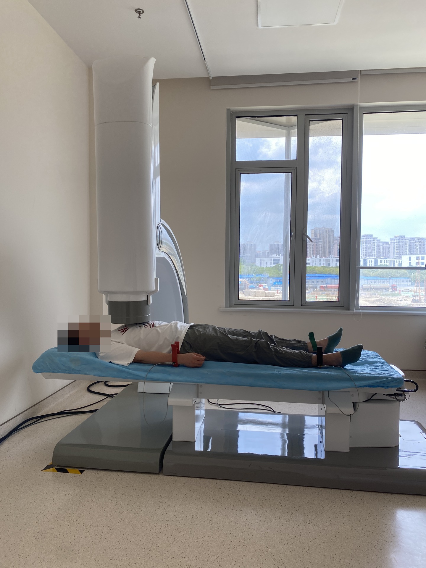 SQUID clinical setting with a detector above the chest and an examination bed; the patient's face is pixelated